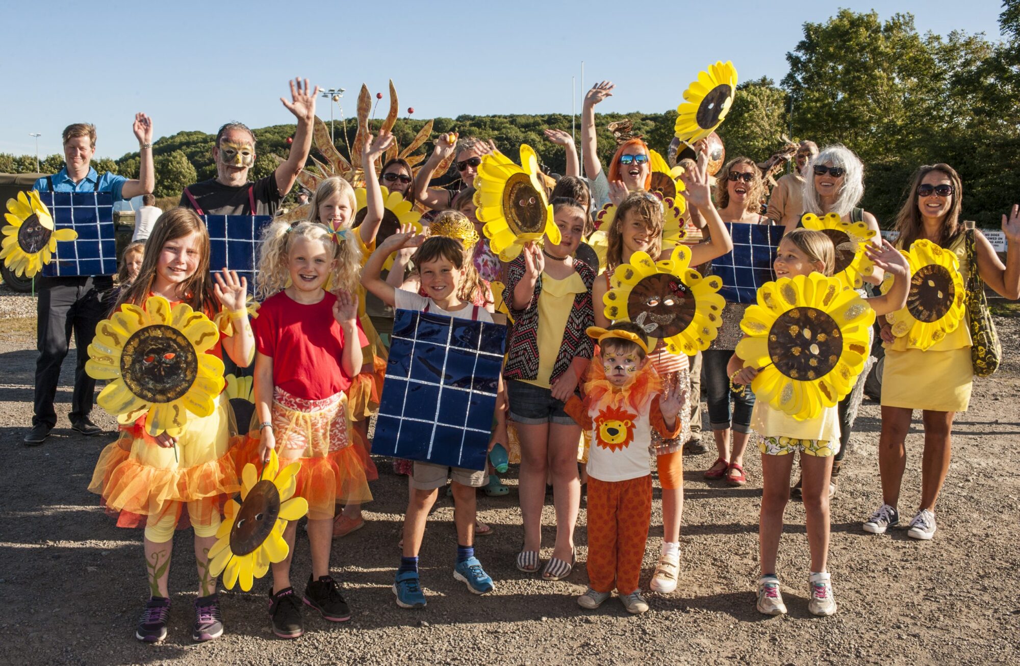 A group of children and young people smiling and holding sunflowers and solar panels at an event organised by Wadebridge Renewable Energy Network (WREN).
